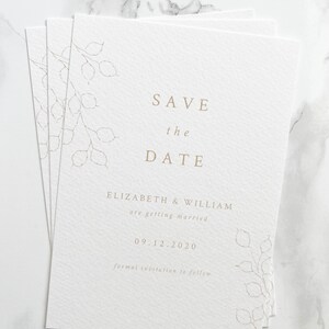 Pile of save the date cards for autumn or winter wedding. Minimal design with hand drawn lunaria branches and clean serif font design. Printed in pale gold onto white, luxury textured paper.