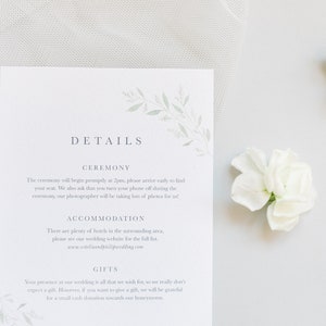 Wedding stationery flat lay with A6 portrait details card. Design features pale green watercolour eucalyptus branches in two opposing corners with minimal text in grey. Printed on luxe white card.