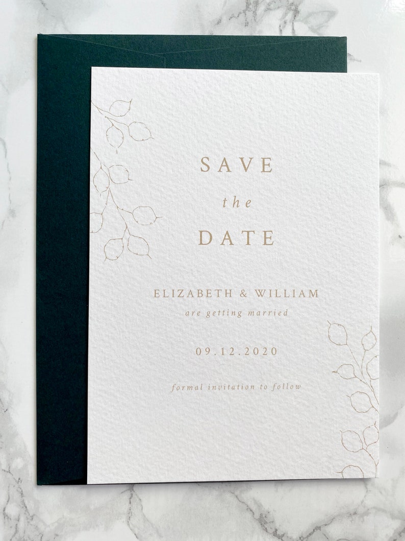 Wedding save the date card with dark green envelope. Modern and minimal design with hand drawn honesty branches in opposite top and bottom corner. Text is centred. Printed in pale gold on luxury white textured paper.