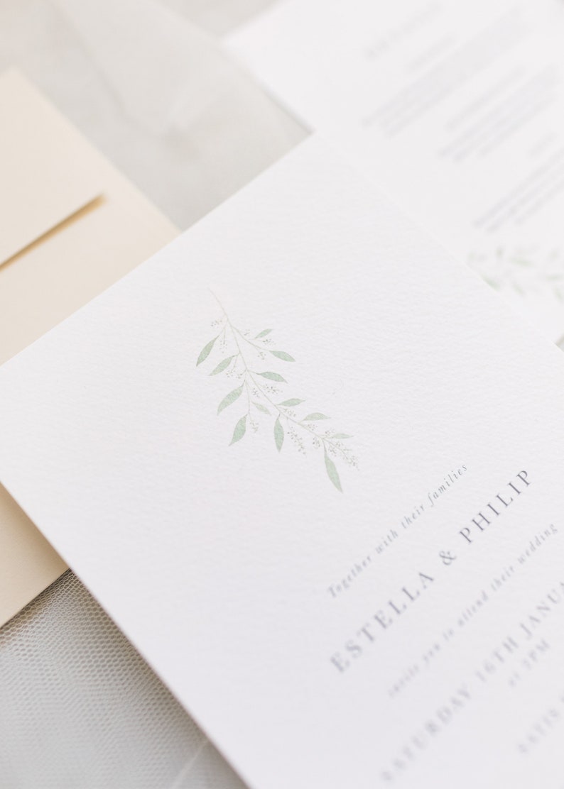 Close up of 5x7 wedding invitation and stone envelope. Invite has simple watercolour branch at the top in pale green with minimal event details below in grey. Printed on luxury white paper with a subtle texture similar to watercolour paper