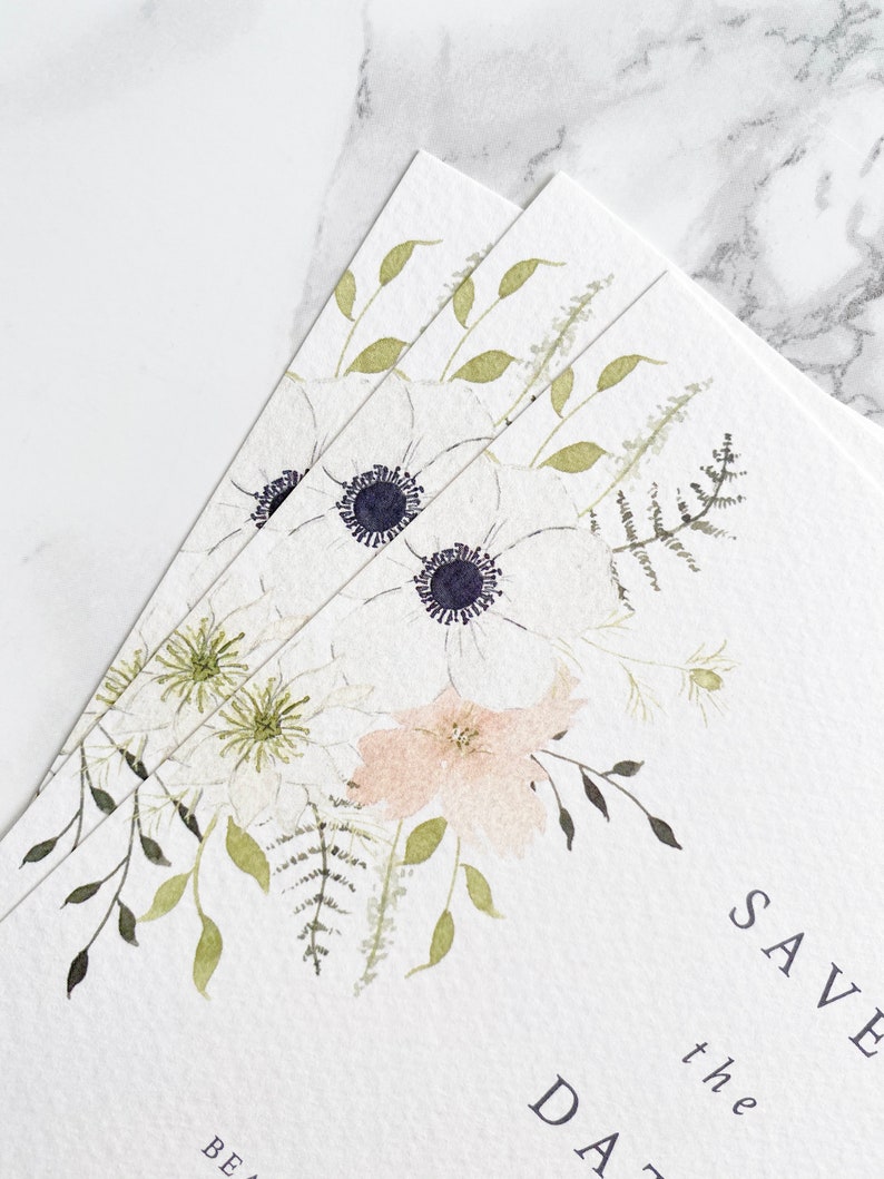 Close up of illustration on A6 save the date card pile. Watercolour floral illustration with white anemone and peach and cream flowers. Save the date is in aligned right in a minimal, modern style. Printed on luxury white textured paper.
