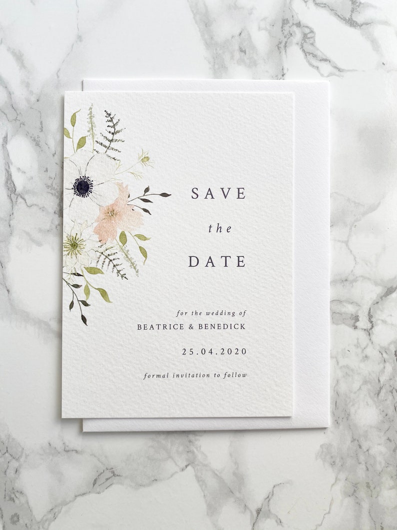 A6 portrait save the date card with white envelope. Design features spring watercolour florals in peach, white and cream with anemone and ranunculus. Minimal design with elegant serif font printed on luxury white textured card stock.