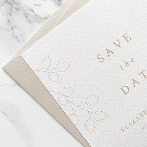 Close up of illustration detail on top corner of wedding save the date card with pale sand coloured envelope. Hand drawn honesty branches in delicate line drawing style with save the date in clean and modern serif font.