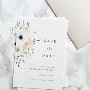 A6 portrait save the date card with spring watercolour florals in peach, white and cream with anemone and ranunculus. Minimal design with elegant serif font printed on luxury white textured card stock. Envelope is a neutral stone colour.