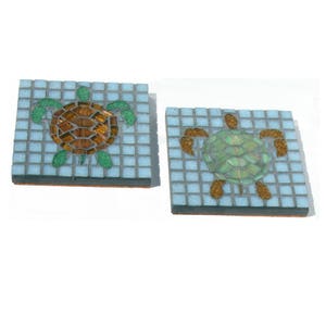 May include: Two square ceramic coasters with a mosaic design of sea turtles. One turtle is brown and green, the other is green and gold.