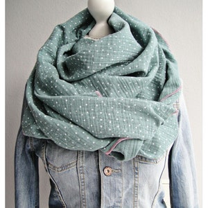 Könnte beinhalten: Ein weicher, grün-weißer Tüllschal mit rosa Saum. Der Schal ist gefaltet und um den Hals einer Puppe gelegt.