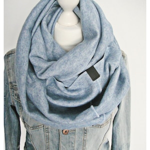Könnte beinhalten: Ein hellblauer Infinity-Schal aus weichem, strukturiertem Stoff. Der Schal wird von einem Mannequin mit einer Jeansjacke getragen.