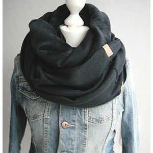 Könnte beinhalten: Ein schwarzer Fleece-Infinity-Schal mit einem braunen Leder-Etikett. Der Schal wird über einer Jeansjacke getragen.