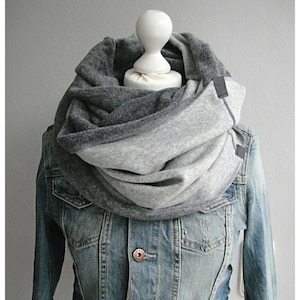 Könnte beinhalten: Ein grauer und hellgrauer Infinity-Schal aus weichem Fleece-Stoff. Der Schal wird von einem Mannequin getragen, das eine Jeansjacke trägt.