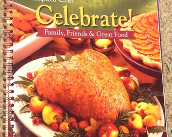 May include: A cookbook titled "The Pampered Chef Celebrate! Family, Friends & Great Food" with a photo of a roasted turkey breast on a white platter surrounded by apples and cranberries.