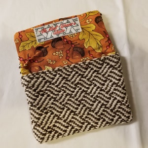 Op de afbeelding: Een kleine, opgevouwen stoffen etui. De bovenklep heeft een herfstthema met eikels en bladeren op een oranje achtergrond. Het onderste gedeelte heeft een bruin en crèmekleurig visgraatweefsel. Het label luidt "The Mill Weaver's Studio."