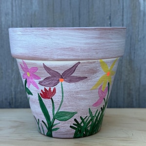 May include: A white terracotta flower pot with hand-painted flowers in shades of pink, purple, yellow, red, and green.