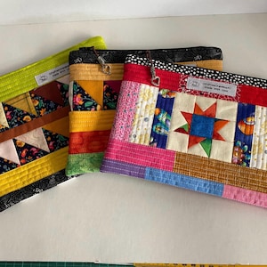 May include: Three colourful quilted zipper pouches. The pouches feature patchwork designs with floral, geometric, and star patterns. Each pouch has a different colour zip and a small metal charm. The pouches are handmade and have a label that says "Made with Love."