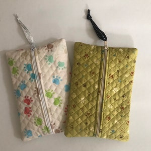 May include: Two quilted zippered pouches with paw print designs. One pouch is white with multi-coloured paw prints and the other is green with brown paw prints.