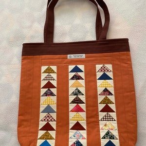 May include: A brown tote bag with a patchwork design of colourful triangles. The bag has brown straps and a label that reads "OriginalHandmade" and "Made with Love".