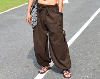 May include: A woman wearing a black crop top with a silver necklace and brown, loose-fitting pants. She is carrying a gray and white patterned bag over her shoulder.