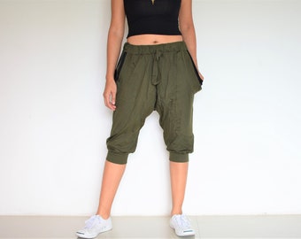 May include: A pair of olive green, cropped,  loose-fitting pants with black trim. The pants have a drawstring waist and a baggy,  relaxed fit.