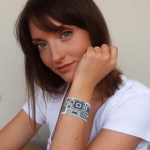 May include: A woman wearing a white shirt with a blue and white beaded bracelet on her wrist.