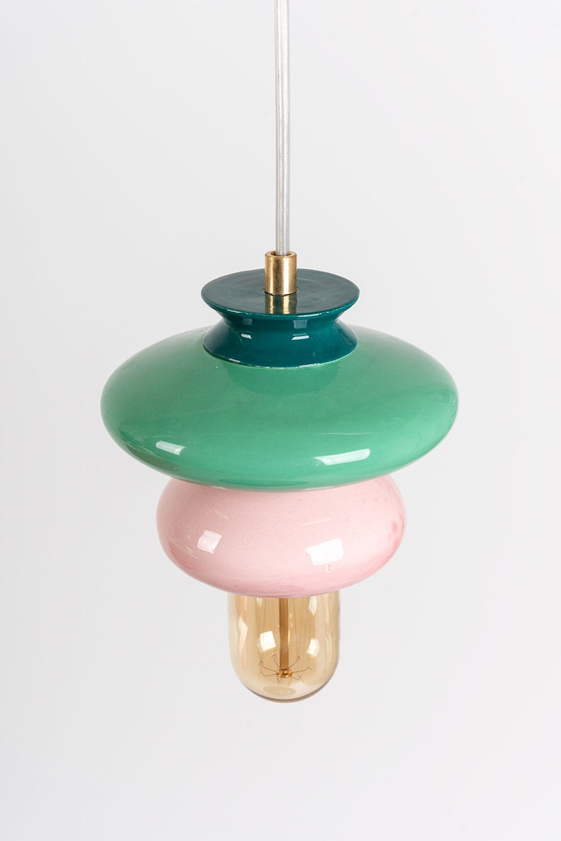 May include: A modern pendant light with three tiers. The top tier is a green saucer, the middle tier is a pink sphere, and the bottom tier is a clear glass bulb.