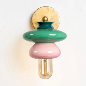 Könnte beinhalten: Eine Wandleuchte aus Keramik in Grün, Rosa und Gold mit runder, bauchiger Form. Die Leuchte hat eine einzelne Glühbirne.