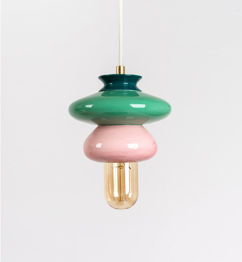 May include: A green, pink, and teal ceramic pendant light with a gold top and a clear light bulb.