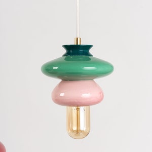 May include: A green, pink, and gold pendant light fixture with a round, layered design. The light fixture has a clear cord and a gold bulb.