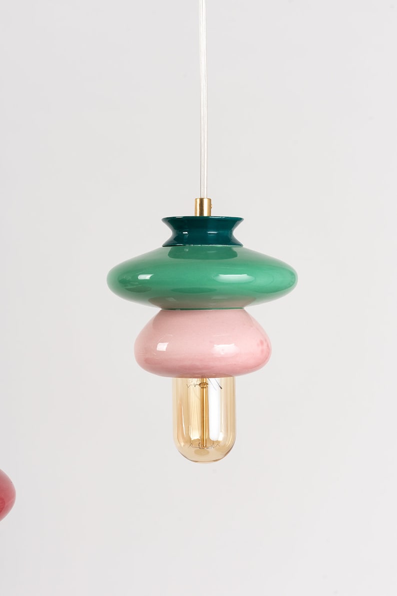 May include: A green, pink, and gold pendant light fixture with a round, layered design. The light fixture has a clear cord and a gold bulb.