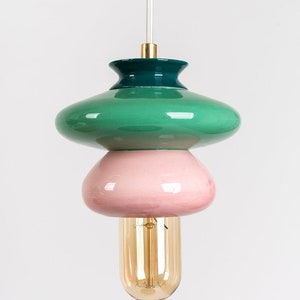 May include: A green, pink, and gold ceramic pendant light with a round, bulbous shape. The light is suspended from a thin wire.