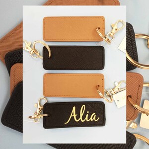 May include: Four leather keyrings with gold rings and clasps. Two keyrings are brown and two are black. One black keyring has the name "Alia" written in gold lettering.