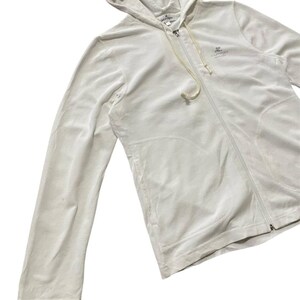 May include: A white zip-up hoodie with a drawstring and a small logo on the chest. The hoodie is made of a soft, velvety material and has a hood. The zipper runs down the front of the hoodie.