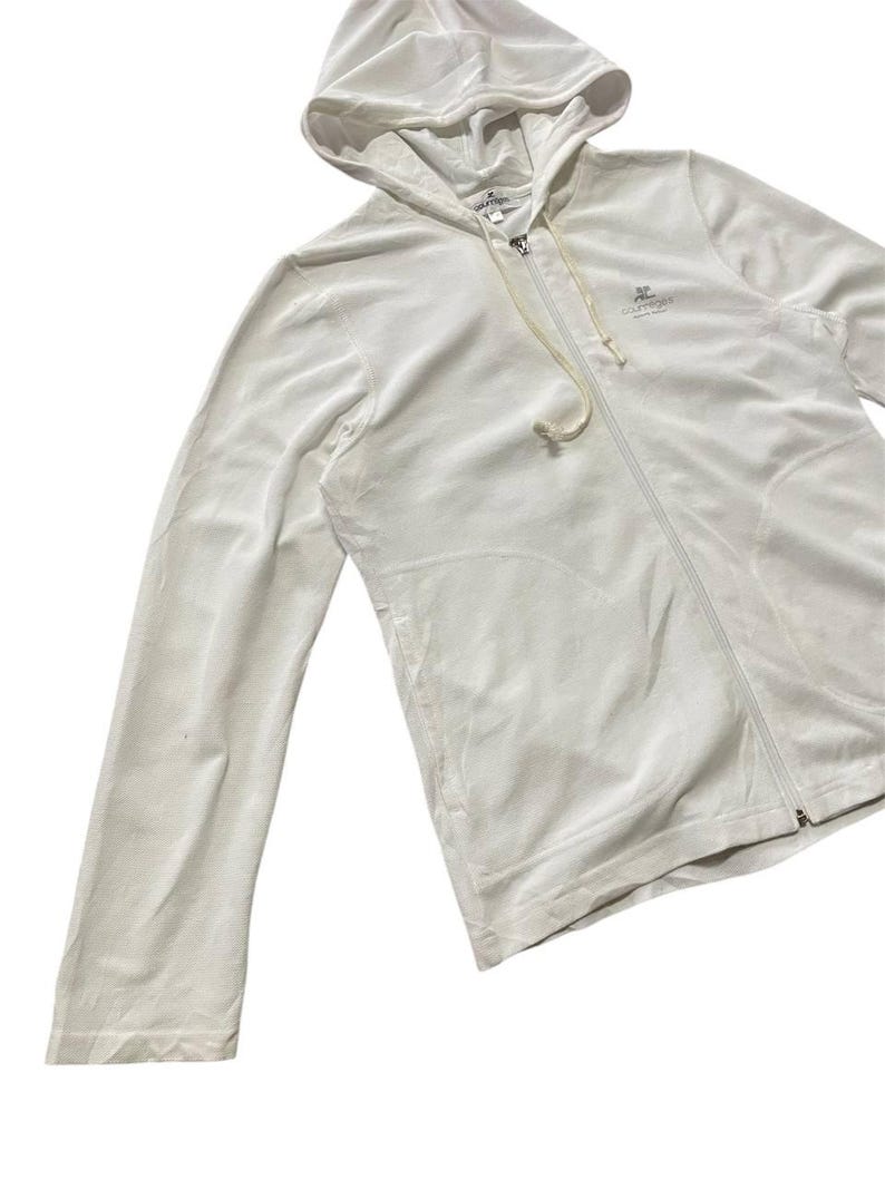 May include: A white zip-up hoodie with a drawstring and a small logo on the chest. The hoodie is made of a soft, velvety material and has a hood. The zipper runs down the front of the hoodie.