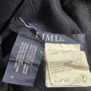 Op de afbeelding: Close-up van zwarte stof met aangehechte labels. E&eacute;n label leest "LIMI feu" en "S". Een ander label geeft aan dat de stof 100% rayon is en wasvoorschriften bevat. De labels zijn aan het kledingstuk bevestigd.