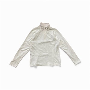 May include: A long-sleeved, off-white top with a mock neck and a quarter-length zipper. The top has a subtle, textured pattern and is laid flat on a white surface. The sleeves are long and the overall style is casual.