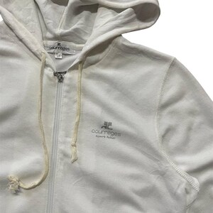 May include: A white zip-up hoodie with a drawstring hood. The hoodie features the brand name "courreges" in a gray font on the chest. The fabric appears to be a textured knit. The zipper is silver.
