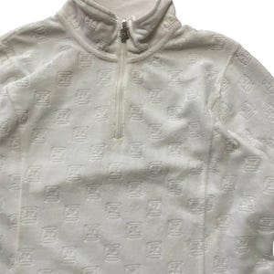 May include: White fleece pullover with a high collar and a quarter-zip closure. The fabric is patterned with a repeating embossed design. The zipper pull is silver. The garment has a soft, textured appearance.