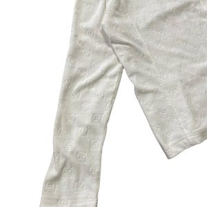 May include: White long-sleeved top with a repeating embossed pattern. The fabric appears to be soft and textured. The top has a zipper detail at the neckline and a fitted sleeve.