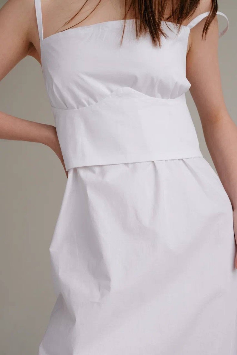 May include: A white sleeveless dress with a fitted bodice and a flowing skirt.