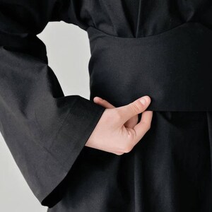 May include: A black long-sleeved dress with a wide, black belt. The dress has a loose, flowing fit and a simple, elegant design.