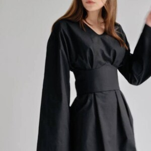 May include: A black long-sleeved dress with a fitted waist and a flowing skirt. The dress has a v-neckline and a simple design.
