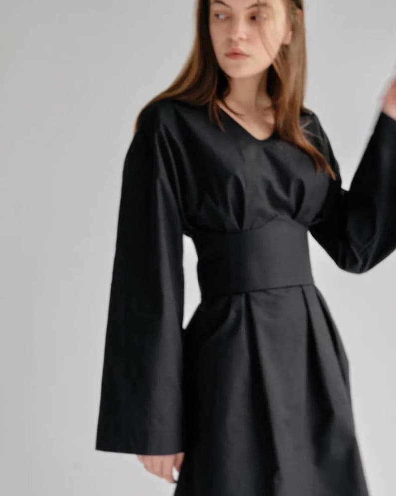 May include: A black long-sleeved dress with a fitted waist and a flowing skirt. The dress has a v-neckline and a simple design.