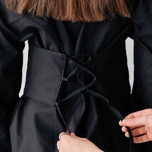 May include: A black shirt with a black corset-style belt that laces up at the back.