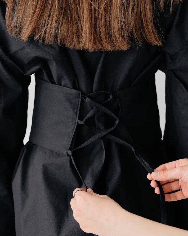 May include: A black shirt with a black corset-style belt that laces up at the back.