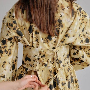 May include: A yellow and brown patterned dress with a black lace-up corset belt. The corset is being tied by two hands.