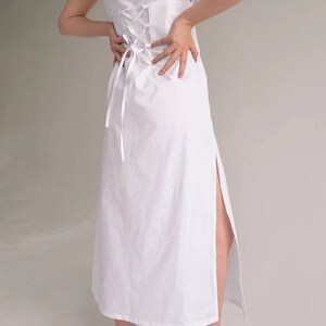 May include: A white maxi dress with a lace-up back detail and a side slit. The dress is made from a lightweight fabric and has a relaxed fit.