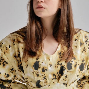 May include: A woman wearing a long-sleeved blouse with a yellow and black abstract print. The blouse has a V-neck and a fitted waist.