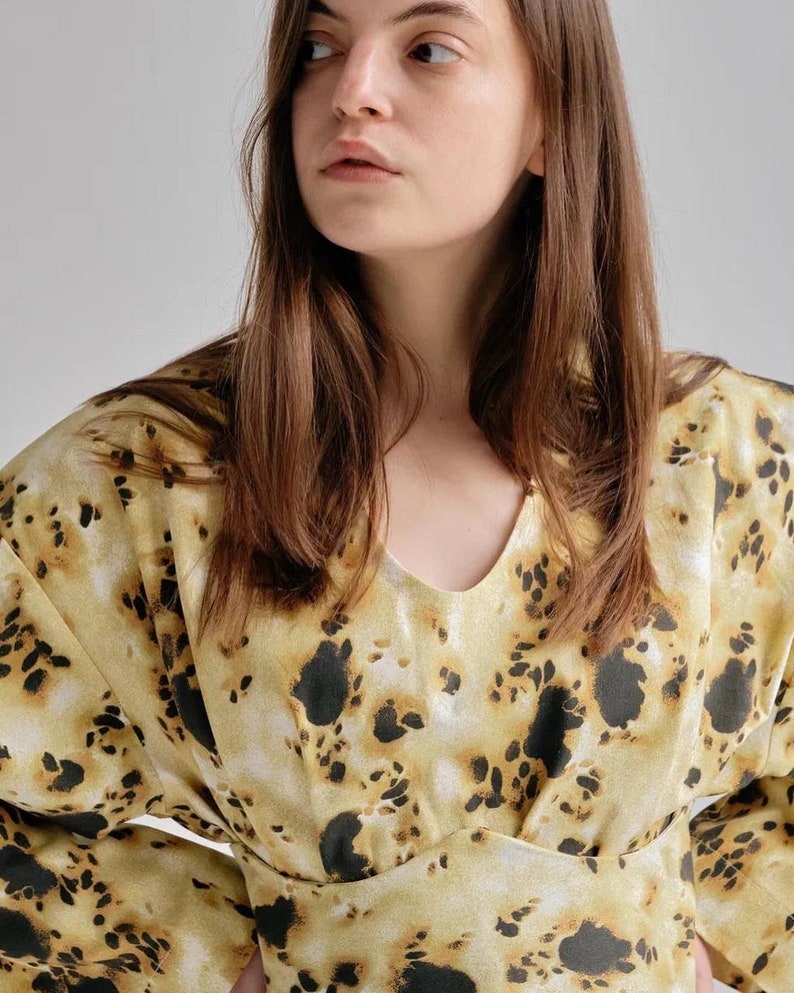 May include: A woman wearing a long-sleeved blouse with a yellow and black abstract print. The blouse has a V-neck and a fitted waist.