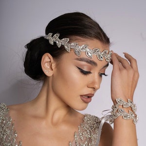 Könnte beinhalten: Eine Frau trägt ein glitzerndes, silbernes und beiges Kleid mit einem silbernen Blattkranz und einem passenden Armband.