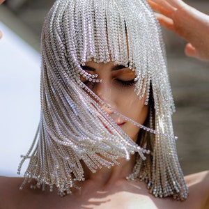Könnte beinhalten: Eine Frau trägt ein silbernes Haarteil mit Fransen aus Strasssteinen. Die Fransen bedecken ihr Gesicht und das Haarteil ist wie ein Bob gestylt.