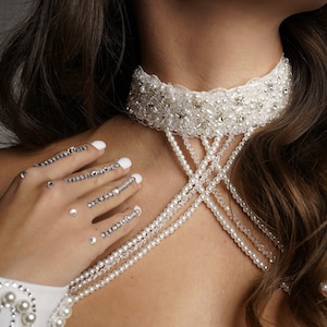 Op de afbeelding: Een witte kralen choker met een delicate kantversiering. De ketting heeft meerdere rijen parels en kristal accenten.