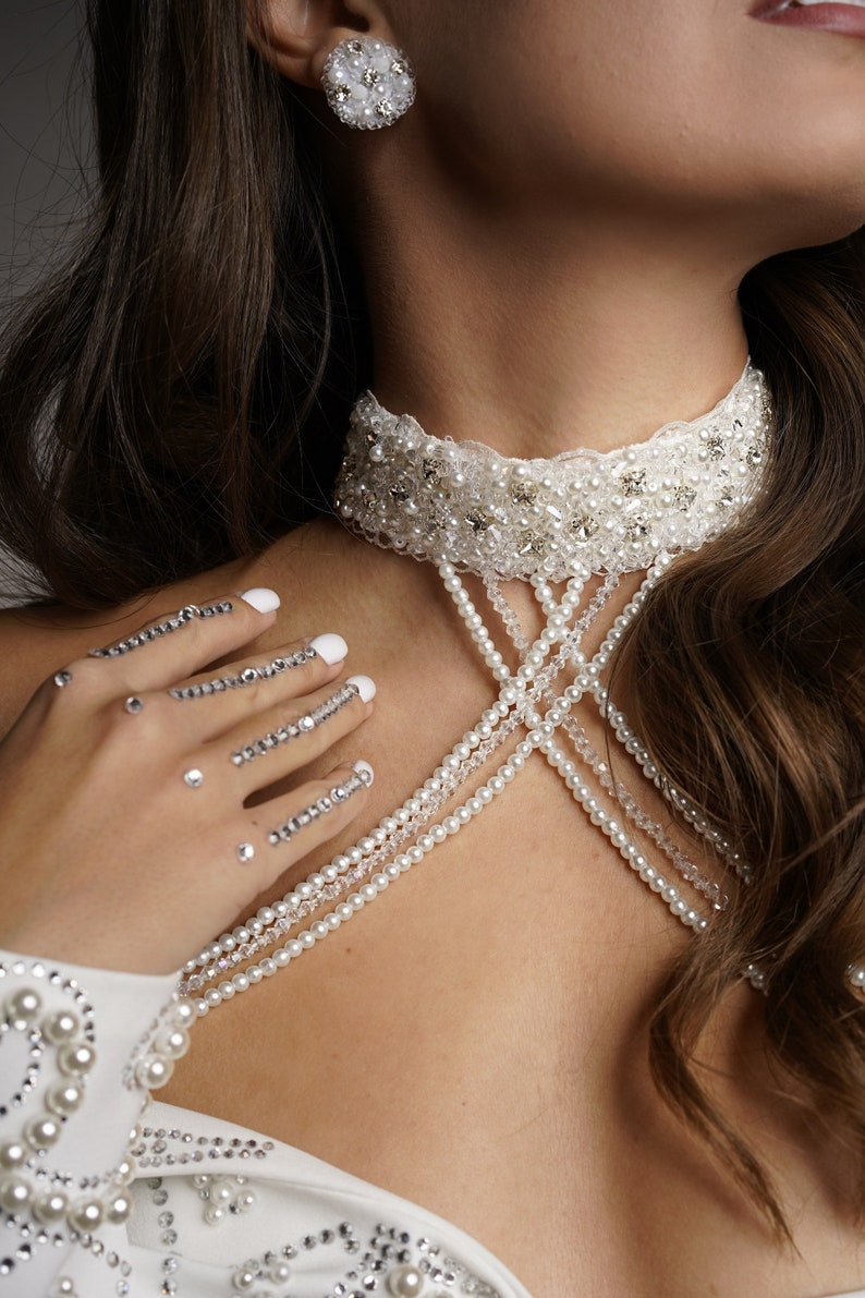 Op de afbeelding: Een witte kralen choker met een delicate kantversiering. De ketting heeft meerdere rijen parels en kristal accenten.